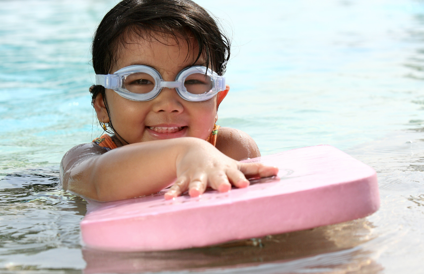 Preschool aged child in water with kickboard wearing googles. 